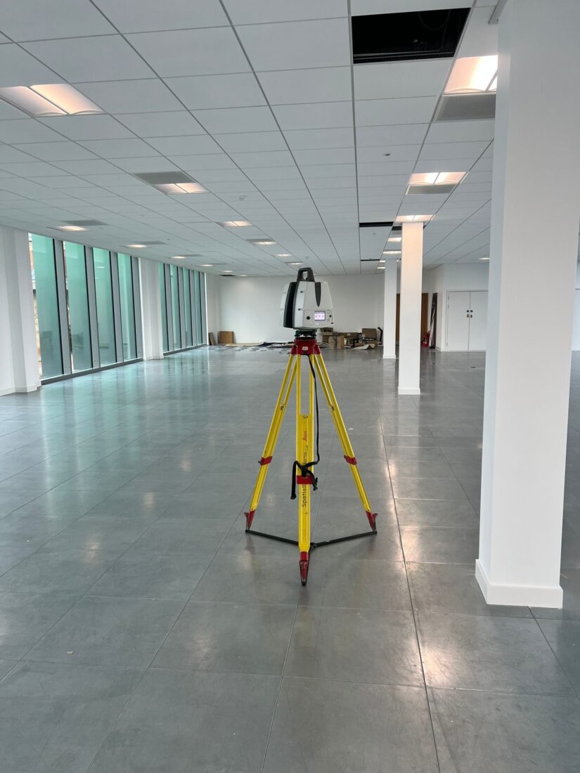 Laser scanner recording an open-plan office interior stripped out for refurbishment, with one suspended ceiling tile removed